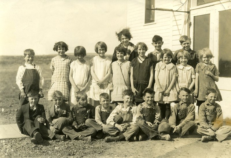 1930sprints004.jpg - Mom is the third child from the left standing. Unfortunately, she lowered her head a bit when the photo was taken. She looks to be about ten, don't you think? That would make this 1931 or so.""Get dressed up today, child!"" mothers say. ""Your getting your picture taken today!""The girls put on their best dresses - do they all look handmade? Most boys wore a clean pair of overalls. Looks like a couple boys were from well-to-do families, as they sport fine suits complete with vests and neckties.And does the school teacher with frazzled hair appear that way because the North Dakota prairie winds are blowing, or because she has a bunch of hellions for students? How many times do you think one of those boys but a bull frog in her desk drawer?!