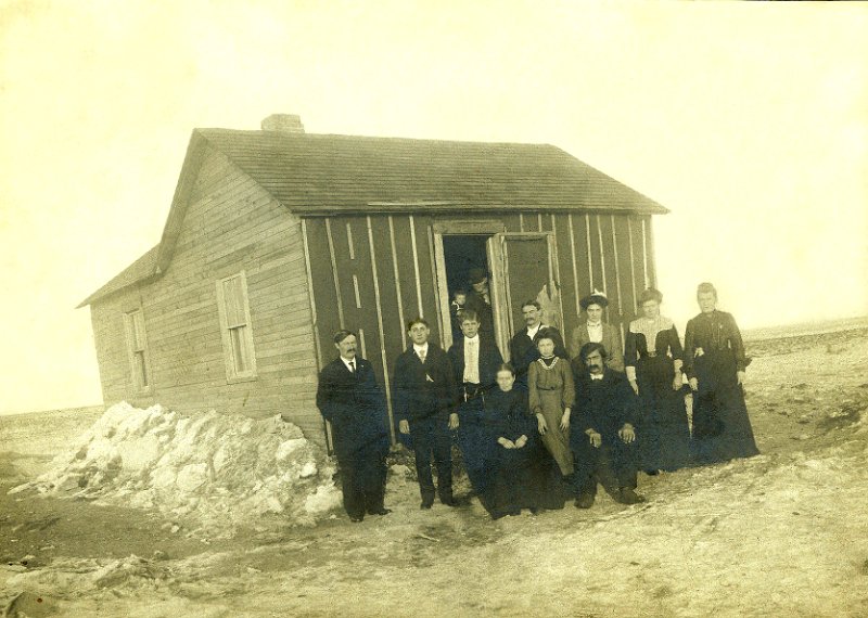 jz_045cropped.jpg - John Zeltinger homestead house. Back row, left to right, Ignatius Zeltinger, Frank Dahinden, Joe Dahinden, John Zeltinger, Mrs. John Zeltinger (nee Anna Dahinden), Mrs. Jim Jensen (nee Magdelena "Kate" Zeltinger), Mary Zeltinger. Front row: Mrs. Xavier Dahinden (formerly Magdelena (nee Haller) Zeltinger), Magdelena "Lena" Dahinden, Xavier Dahinden. Unknowns in doorway.