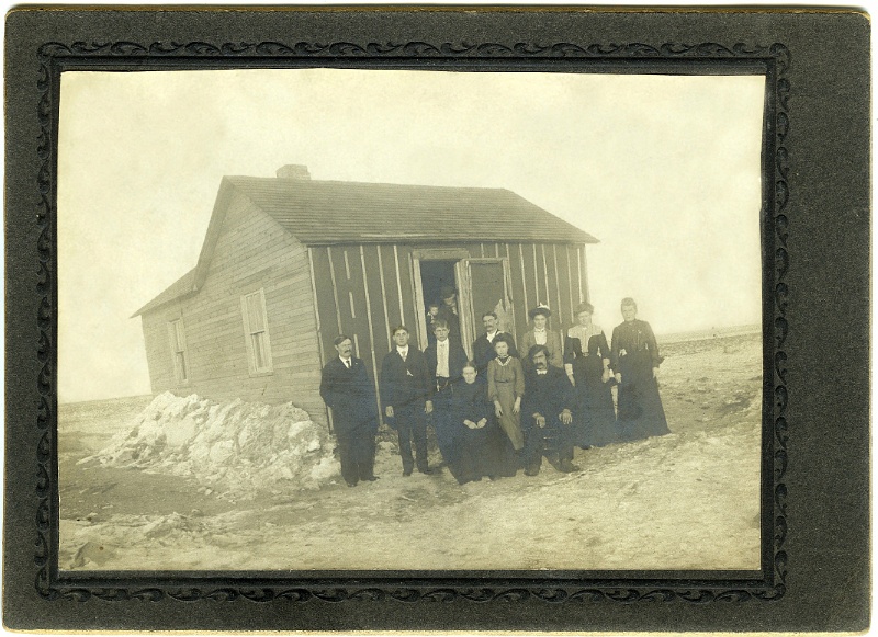 jz_045.jpg - John Zeltinger homestead house. Back row, left to right, Ignatius Zeltinger, Frank Dahinden, Joe Dahinden, John Zeltinger, Mrs. John Zeltinger (nee Anna Dahinden), Mrs. Jim Jensen (nee Magdelena "Kate" Zeltinger), Mary Zeltinger. Front row: Mrs. Xavier Dahinden (formerly Magdelena (nee Haller) Zeltinger), Magdelena "Lena" Dahinden, Xavier Dahinden. Unknowns in doorway.