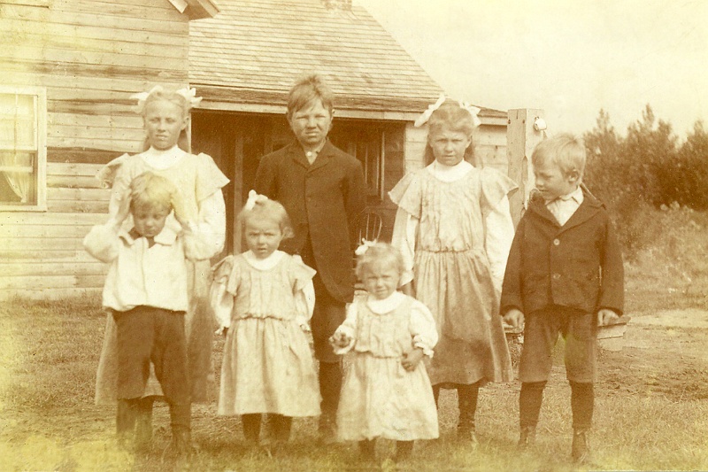 zeltinger002.jpg - These are seven of the twelve children born of Ignatius and Katie (nee Ethen) Zeltinger. Back Row: Lena, Mathias (aka Math, Matt), Louise, Frank; Front Row: John, Clara, Ann. From a family history: Great grandfather Ignatius (1871-1952) was a school teacher in Spring Hill, MN. Grandfather Matt was  born there as were two other siblings. In June, 1900 Ignatius, his brother, John Zeltinger, and his brother-in-law, Henry Ethen, took a train to Kenmare, ND where they disembarked and walked to land where they staked their claims (in Roosevelt Township south of where Tolley, ND was later built). After filing their claims, they returned to MN, but returned to their land later that summer to build their claim shacks (required to be built when homesteading). The three men dug a well, made hay for the horses, and built several sod barns while waiting for their parents, wives and children to arrive. In November, 1900 the group arrived bringing with them a carload of supplies, several horses, chickens, a cow, and lumber for the house on Ignatius' claim, where all of them stayed for the first winter. (While building this house, the group stayed at the Joseph Weber home not far away. The Webers were from St. Cloud, MN and had arrived earlier that year.)During the first year, supplies were gotten from Kenmare, ND which was about 14 miles away. The nearest Doctor was also in Kenmare. Wheat was taken to be ground at McKinney, ND, about 6 miles away.The original Ignatius Zeltinger house (four rooms and a loft) housed the family until 1916. At that time, it was replaced by a house that still stands. This new house was the first farm house in the area to have indoor plumbing and hot water heating.The attached photo is taken in front of the first house. It was built in 1900-1. Matt appears to be 13 years of age, or so. He was born in 1897, so this photo, I estimate, was taken in 1910. Notice the enameled drinking cup hanging on the outdoor water pump. The pump handle sticks out a little above Frank's left shoulder. There is a chair on the back porch along with some hanging yard tools. Curtains in the window. House is unpainted.Matt would live to be 65, dying in 1962 in Pierre, SD.